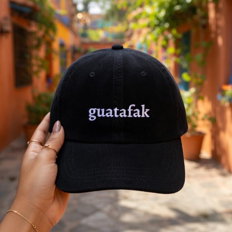 May include: Black baseball cap with the word "guatafak" embroidered in white. The cap has a curved brim and a fabric strap closure. A casual accessory for everyday wear.