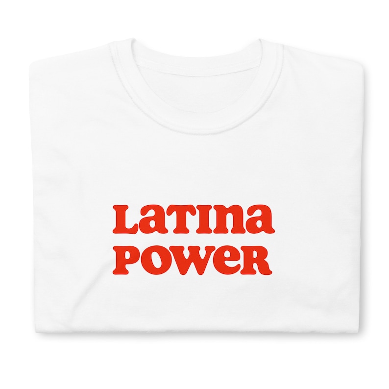 以下が含まれることがあります： 「Latina POWER」の文字が赤色の太字でプリントされた白いTシャツ。 レトロで丸みを帯びたフォントを使用。 Tシャツはきれいに折りたたまれ、デザインが際立っています。