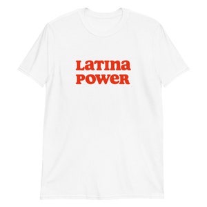 以下が含まれることがあります： 「Latina Power」の文字が赤色の太字でプリントされた白いTシャツ。テキストはシャツの前面中央に配置されています。このシャツは半袖で、クルーネックです。