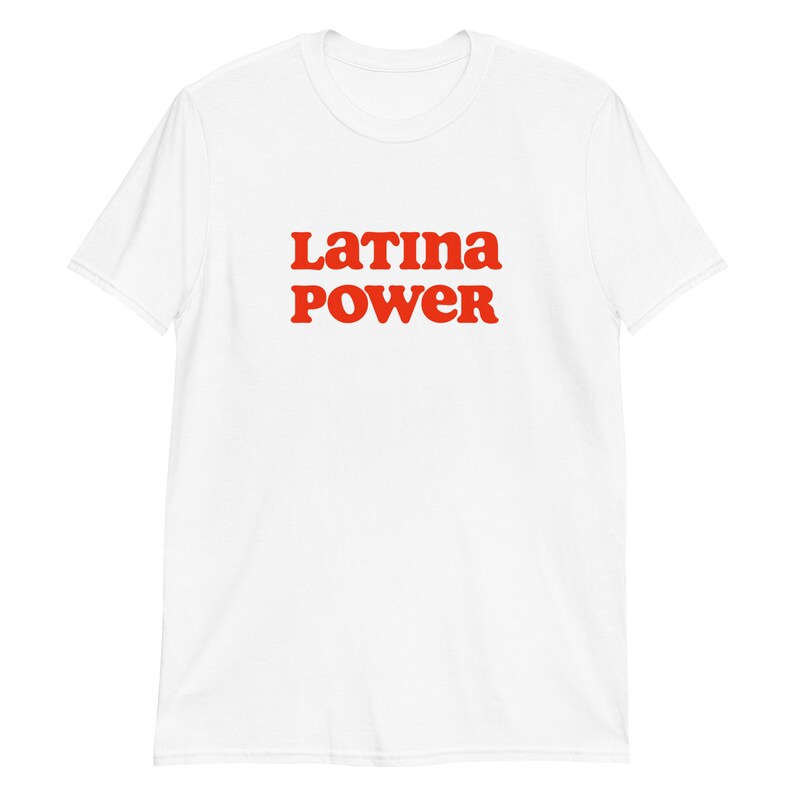 以下が含まれることがあります： 「Latina Power」の文字が赤色の太字でプリントされた白いTシャツ。テキストはシャツの前面中央に配置されています。このシャツは半袖で、クルーネックです。