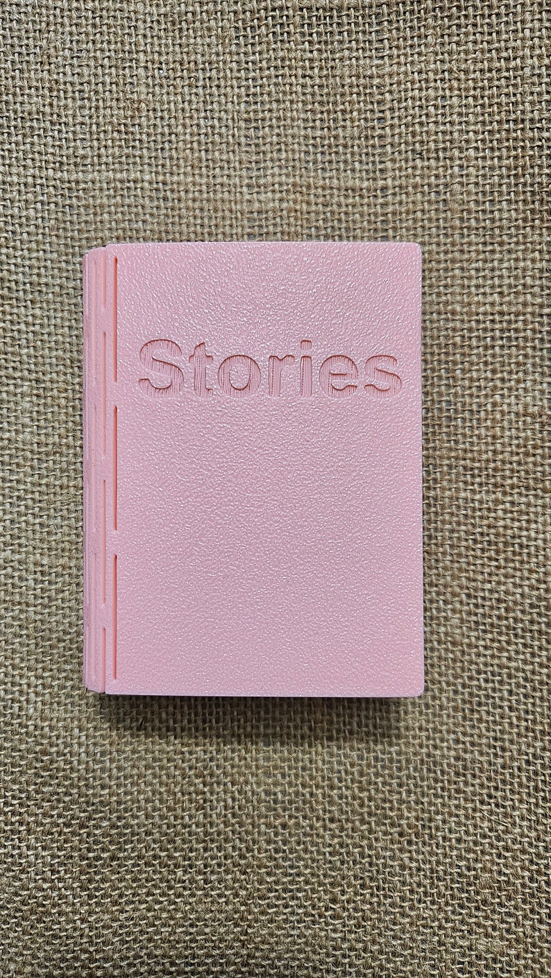 3d printed storage box for holding Yoto cards. Designed to look like a book,this one is Pink with white pages and has the word "Stories" on the front. This can be fully customised.