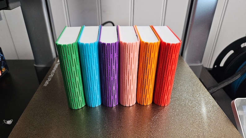 Selection of 3d printed storage boxes for holding Yoto cards. They are designed to look like a book, have a colour cover, white pages, and can be customised with any text.