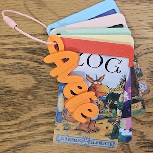 May include: A set of stacked, rectangular plastic cards featuring illustrations from the book Zog by Julia Donaldson and Axel Scheffler. The cards are held together by a pink wire loop and a bright orange 3D-printed name tag reading Janelle.