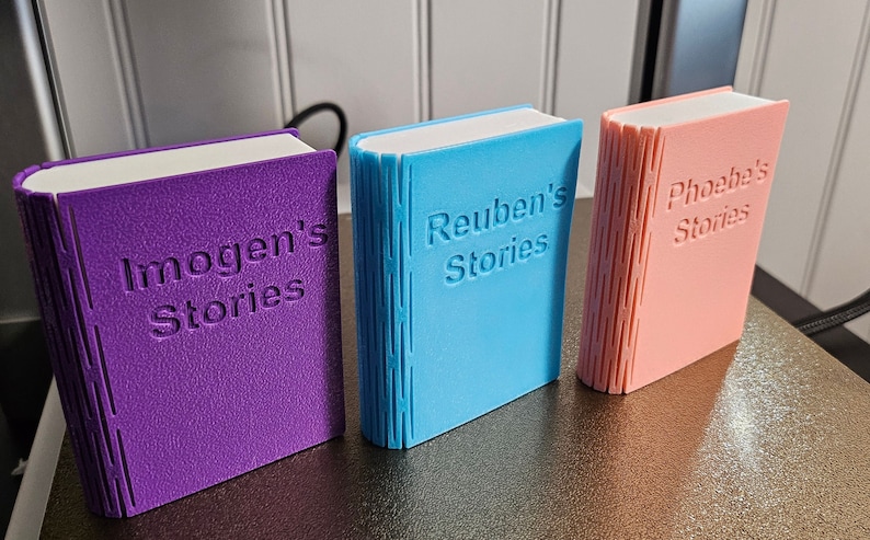 3d printed storage boxes for holding Yoto cards. Designed to look like a book, these ones are Pink, Purple and Blue with white pages and has each has a customised cover bearing the name of the owner. This can be fully customised.