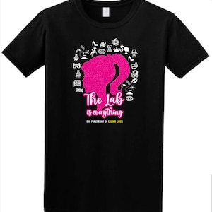 Op de afbeelding: Zwart T-shirt met een roze silhouet van een vrouwenhoofd omringd door wetenschappelijke iconen. De tekst "The Lab is everything" staat onder het silhouet, met de kleinere tekst "THE FOREFRONT OF SAVING LIVES" eronder.