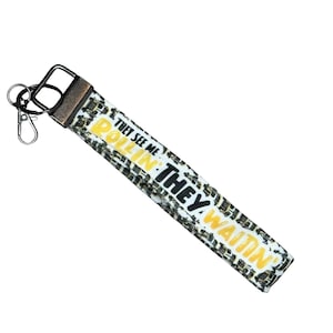 May include: A white and black patterned wrist lanyard with the text "THEY SEE ME ROLLIN' THEY HATIN'". The lanyard has a metal clasp and key ring.