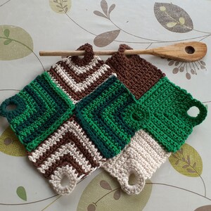 May include: Two crocheted pot holders with a brown, white and green striped pattern. The pot holders have a loop on each side for hanging.