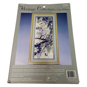 May include: A Heritage Collection stitchery kit titled Enchanted April by Elsa Williams. The packaging features a white heron perched on a branch with purple flowers. Finished size is 10 inches by 24 inches, frame size is 14 inches by 28 inches.