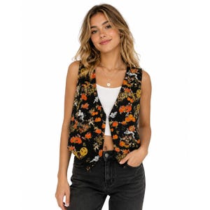 May include: A sleeveless vest featuring a black base with an all-over print of orange pumpkins, white ghosts, and yellow stars. The vest has a V-neckline and is worn over a plain white tank top, paired with dark gray denim jeans.