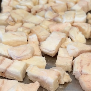 May include: A close-up shot of a tray filled with numerous rectangular pieces of raw, pale-coloured meat. The pieces have a slightly pinkish hue and a fibrous texture, suggesting a cut of meat.