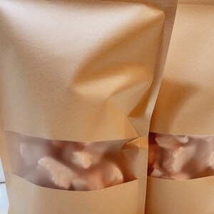 Puede incluir: Dos bolsas de papel marr&oacute;n con ventanas de pl&aacute;stico transparente, cada una con trozos de pollo crudo congelados.