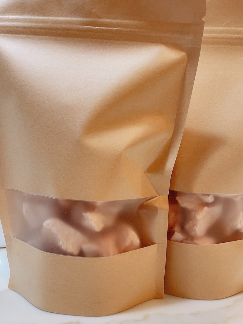 Puede incluir: Dos bolsas de papel marr&oacute;n con ventanas de pl&aacute;stico transparente, cada una con trozos de pollo crudo congelados.