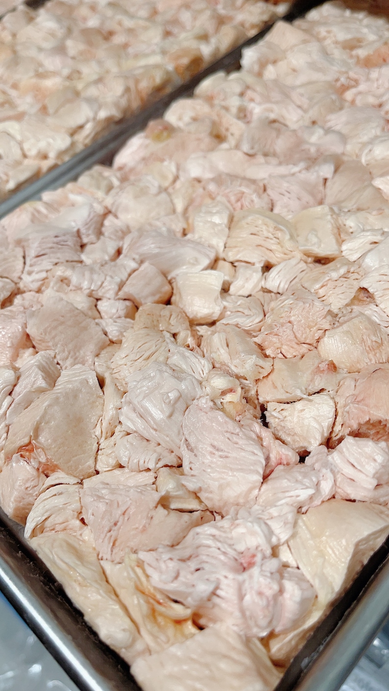 Puede incluir: Primer plano de una bandeja de metal llena de pollo crudo en cubos. El pollo es de color rosa p&aacute;lido y tiene una superficie ligeramente texturizada.