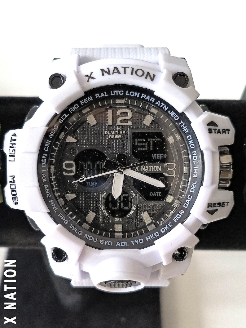 May include: White X Nation digital watch with a black and gray face. The watch features a digital display, analog hands, and various buttons. The watch has the text "X NATION" on the top and the text "DUAL TIME WR 50M" on the face.
