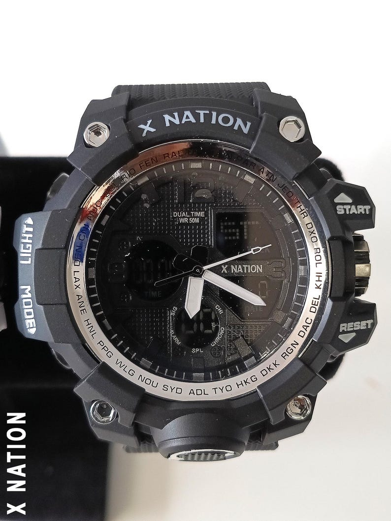 May include: Black digital watch with the text "X NATION" on the face and band. The watch has multiple buttons, including "START" and "RESET". The watch face displays the time and other functions. The watch band is black.