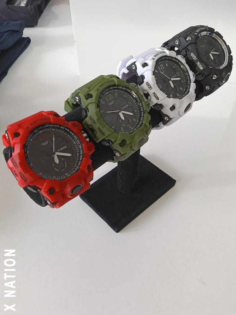 May include: Four digital watches in red, green, white, and black, displayed on a black stand. Each watch has a round face with a black dial and white numerals. The watches have a rugged, sporty design.