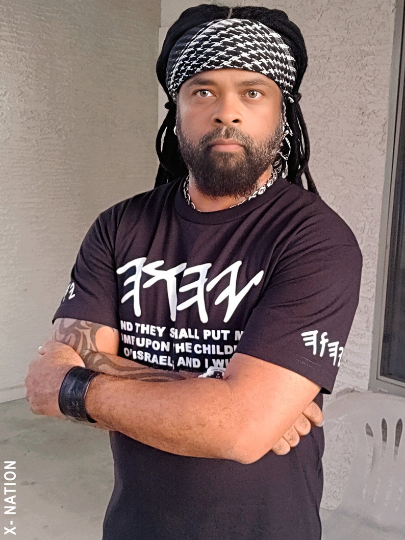 May include: A person wearing a black t-shirt with white Hebrew text and the words "AND THEY SHALL PUT M...ISRAEL, AND I W". The person is also wearing a black and white headscarf and a black wristband.