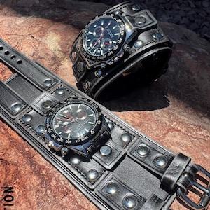 May include: Two black leather wristwatches with silver-tone accents and a chronograph dial. One watch is a cuff style, and the other is a strap style. The watches are on a textured surface. The text "X NATION" is visible.