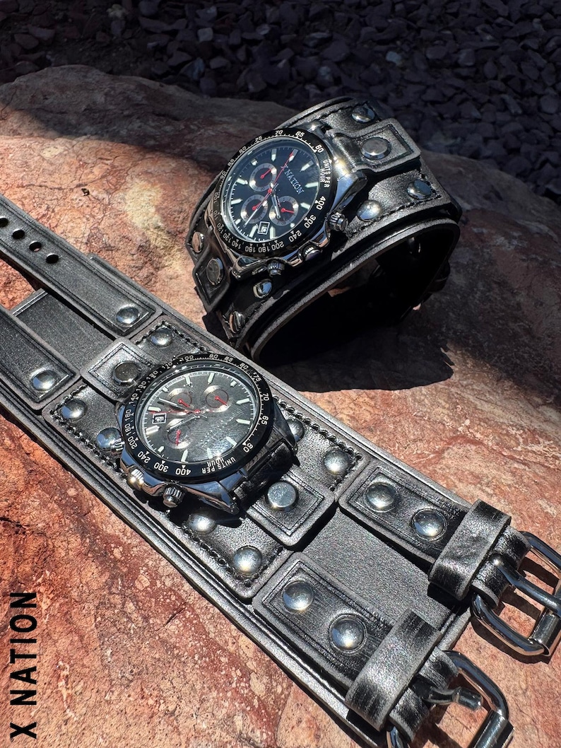 May include: Two black leather wristwatches with silver-tone accents and a chronograph dial. One watch is a cuff style, and the other is a strap style. The watches are on a textured surface. The text "X NATION" is visible.