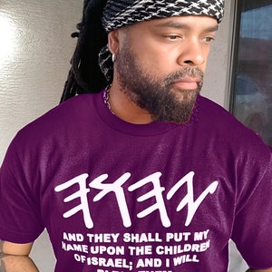 May include: A purple t-shirt with white Hebrew text and the quote "AND THEY SHALL PUT MY NAME UPON THE CHILDREN OF ISRAEL; AND I WILL BLESS THEM. NUMBERS 6:27." The person is wearing a black and white patterned head covering.