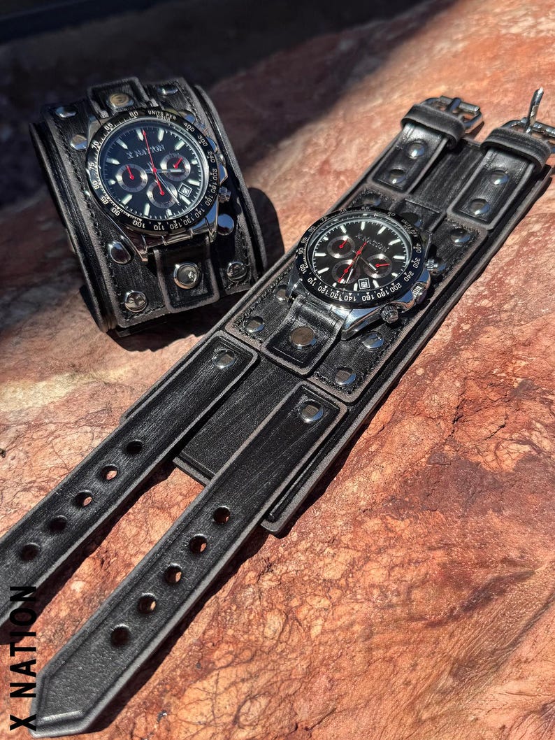 May include: Two black leather wrist cuffs with silver-toned watch faces. The watches have black dials with red accents and silver-toned bezels. The cuffs are riveted and have adjustable straps. The text "X NATION" is visible.