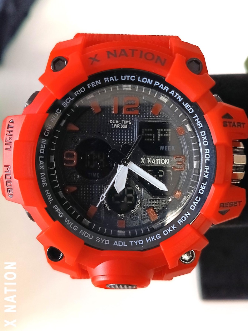 May include: A vibrant orange digital watch with a black face. The watch features the text "X NATION" and various function buttons. The watch face displays the time, day, and other digital readouts. The watch has a sporty, rugged design.