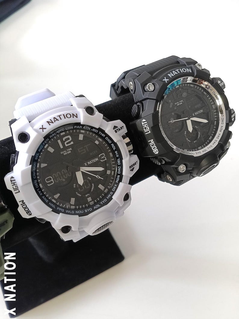 May include: Two digital watches with the text "X NATION" on the face and bezel. One watch is white with a black face, and the other is black with a black face. Both watches have multiple buttons and digital displays.