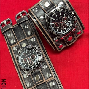 May include: Two black leather wrist cuffs with silver studs and buckles, each featuring a watch with a black face and silver bezel. The watches display the text "X NATION". The cuffs are on a red background.