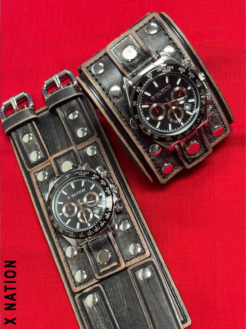 May include: Two black leather wrist cuffs with silver studs and buckles, each featuring a watch with a black face and silver bezel. The watches display the text "X NATION". The cuffs are on a red background.