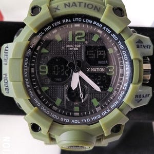 May include: An olive green digital watch with the text "X NATION" on the bezel. The watch face displays the time, day, and date. It has multiple buttons for various functions, including "START" and "RESET".
