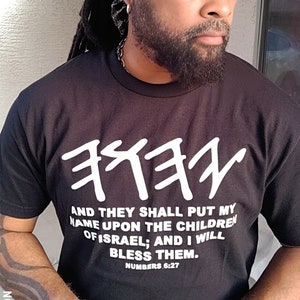 May include: Black t-shirt with white Hebrew text and the quote "AND THEY SHALL PUT MY NAME UPON THE CHILDREN OF ISRAEL; AND I WILL BLESS THEM. NUMBERS 6:27." The shirt has the text "X-NATION" on the side.
