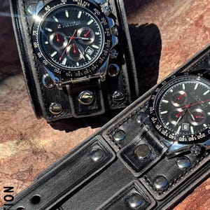 May include: Two black leather wristwatches with silver-tone accents. The watch faces are black with red and silver details. The watch bands are wide, studded leather cuffs. The text "X NATION" is visible on the watch face and band.