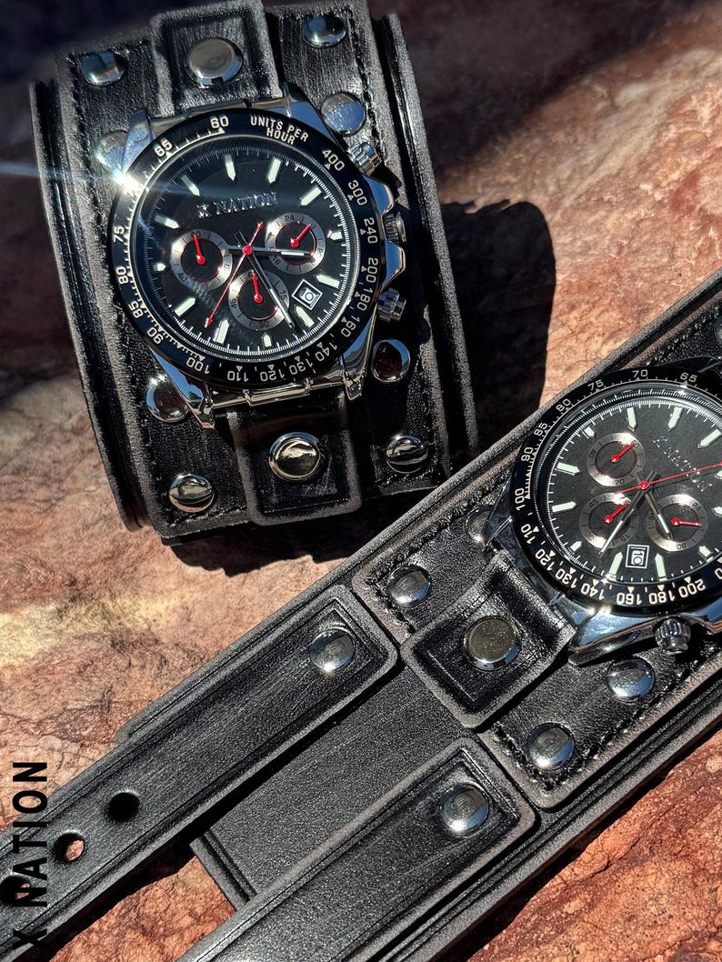 May include: Two black leather wristwatches with silver-tone accents. The watch faces are black with red and silver details. The watch bands are wide, studded leather cuffs. The text "X NATION" is visible on the watch face and band.