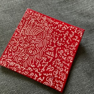 Puede incluir: Un lienzo cuadrado rojo con arte abstracto garabateado en blanco. El arte garabateado es un patrón de líneas, formas y símbolos.