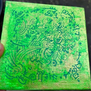 Puede incluir: Pequeño lienzo cuadrado con un fondo verde vibrante y intrincados diseños abstractos verdes. La obra de arte presenta una mezcla de líneas, espirales y símbolos, creando una composición única y llamativa. El lienzo está sostenido por una mano.