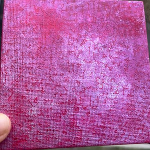 Puede incluir: Pequeño lienzo cuadrado con superficie texturizada. Pintado en tonos rosa y magenta, con pinceladas visibles y un aspecto ligeramente desgastado. La obra de arte tiene una cualidad abstracta y hecha a mano.