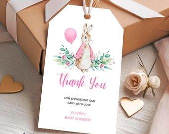 May include: A white rectangular gift tag with a watercolor illustration of a rabbit in a pink jacket holding a pink balloon, surrounded by green leaves. The text reads Thank You, FOR SHOWERING OUR BABY WITH LOVE, OLIVIA'S BABY SHOWER.