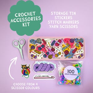 May include: A crochet accessories kit featuring a rectangular pink storage tin with a colorful yarn and hook pattern, light green scissors, three vinyl stickers, and a clear bag containing 100 multicolored plastic stitch markers.
