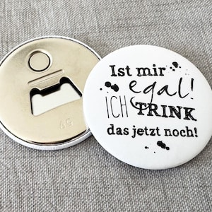 Könnte beinhalten: Ein runder, weißer Flaschenöffner mit dem deutschen Text "Ist mir egal! Ich trink das jetzt noch!" in Schwarz. Der Flaschenöffner ist silberfarben und hat einen Flaschenöffner.