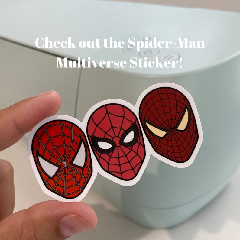 Puede incluir: Una pegatina con tres dise&ntilde;os de m&aacute;scaras de Spider-Man en rojo y negro, con detalles de ojos blancos. El texto "Check out the Spider-Man Multiverse Sticker!" es visible.