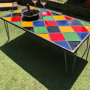May include: A colourful checkered glass top coffee table with black metal legs. The table has a black ice bucket with a bottle of wine and two wine glasses on top.
