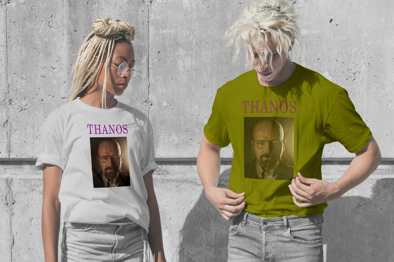 Op de afbeelding: Twee mensen dragen witte en olijfgroene T-shirts met een afbeelding van Walter White uit Breaking Bad en het woord "THANOS" erop.