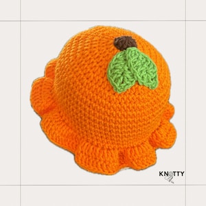 Pu&ograve; includere: Cappello all'uncinetto arancione con un design a foglia verde sulla parte superiore. Il cappello ha un bordo arricciato.