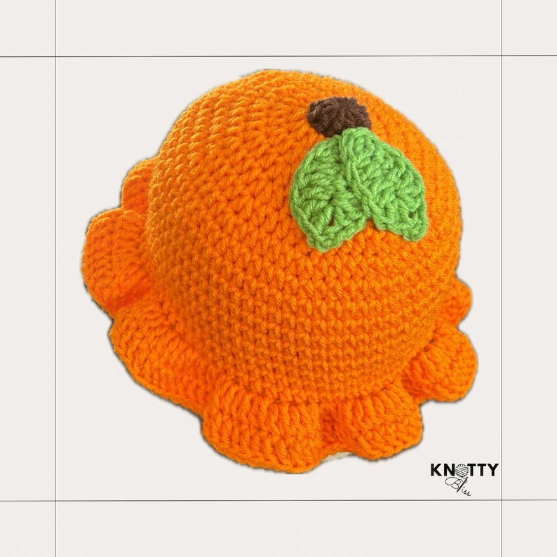 Pu&ograve; includere: Cappello all'uncinetto arancione con un design a foglia verde sulla parte superiore. Il cappello ha un bordo arricciato.