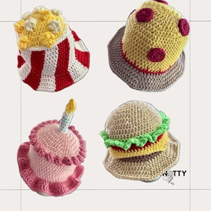 May include: Four crocheted bucket hats featuring food themes: a red and white striped popcorn bucket with yellow kernels, a yellow pizza hat with red pepperoni, a pink birthday cake hat with a candle, and a tan hamburger hat with lettuce.
