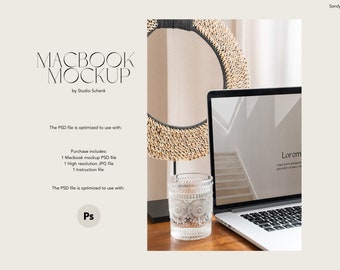 May include: A mockup of a silver Macbook laptop with a white screen displaying a website with the text "Lorem" and a staircase. The laptop is on a wooden table with a glass cup and a decorative round object made of woven material.