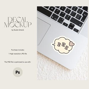 May include: A white laptop with a black keyboard and a white cloud-shaped sticker with the text "zzz" and a small pink heart. The sticker is on the trackpad of the laptop.