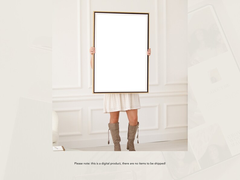May include: A woman is holding a large, blank canvas in a gold frame in front of her. The canvas is white and the frame is a thin, gold metal. The woman is wearing a white dress and brown boots. The background is a white wall with white trim.