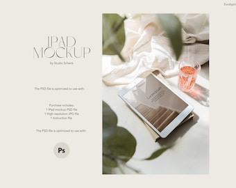May include: A white iPad mockup with a light brown background image of a staircase. The iPad is lying on a stack of books with a glass of pink liquid and a green plant in the background. The text "Lorem Ipsum" is visible on the iPad screen.