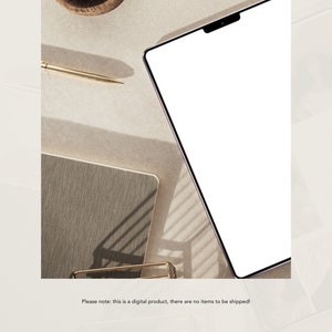 Op de afbeelding: Een witte tabletcomputer met een zwarte rand, liggend op een beige oppervlak met een gouden pen en een notitieboek.